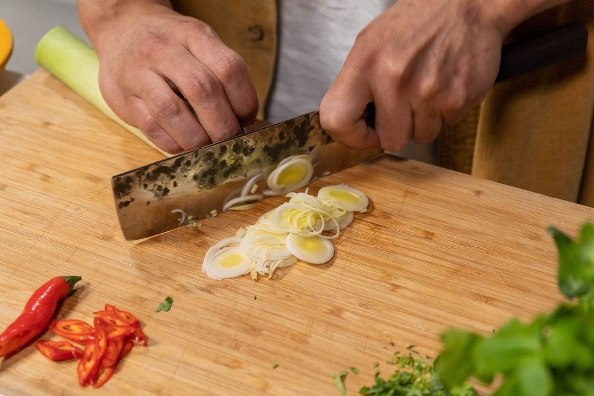 Personne tranchant des oignons sur une planche à découper avec des piments et des herbes à proximité Personne tranchant des oignons sur une planche à découper avec des piments et des herbes à proximité