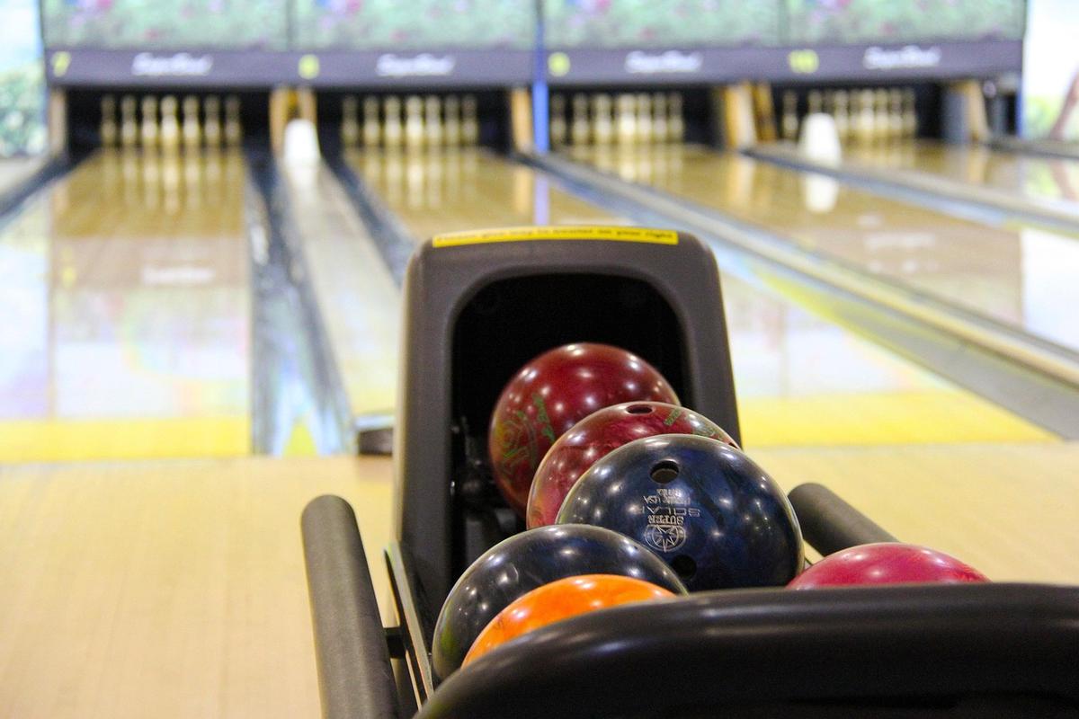 Boules colorées rangées dans un porte-balles, pistes de bowling en arrière-plan Boules colorées rangées dans un porte-balles, pistes de bowling en arrière-plan