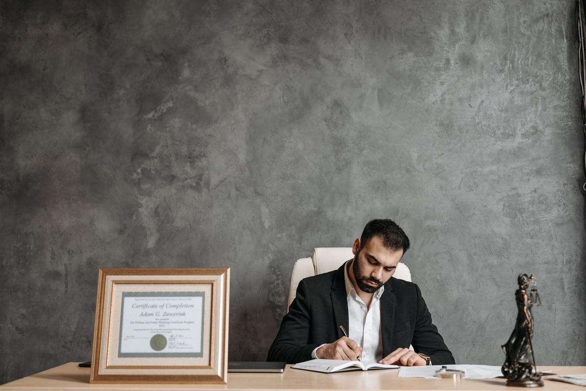 Un homme en costume écrit à un bureau avec un cadre et une statue devant lui
