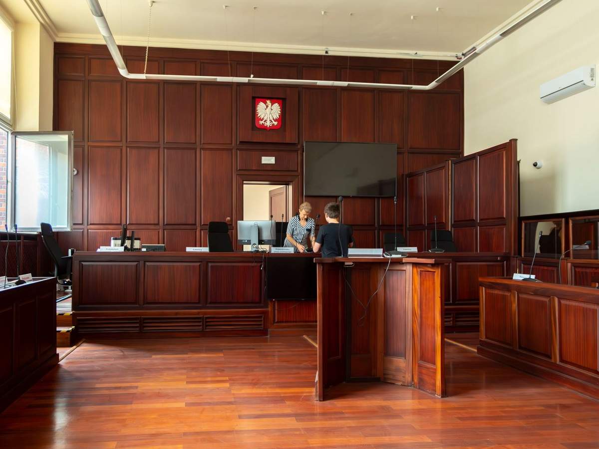 Salle de tribunal en bois avec deux personnes derrière le bureau, écran plat et fenêtres