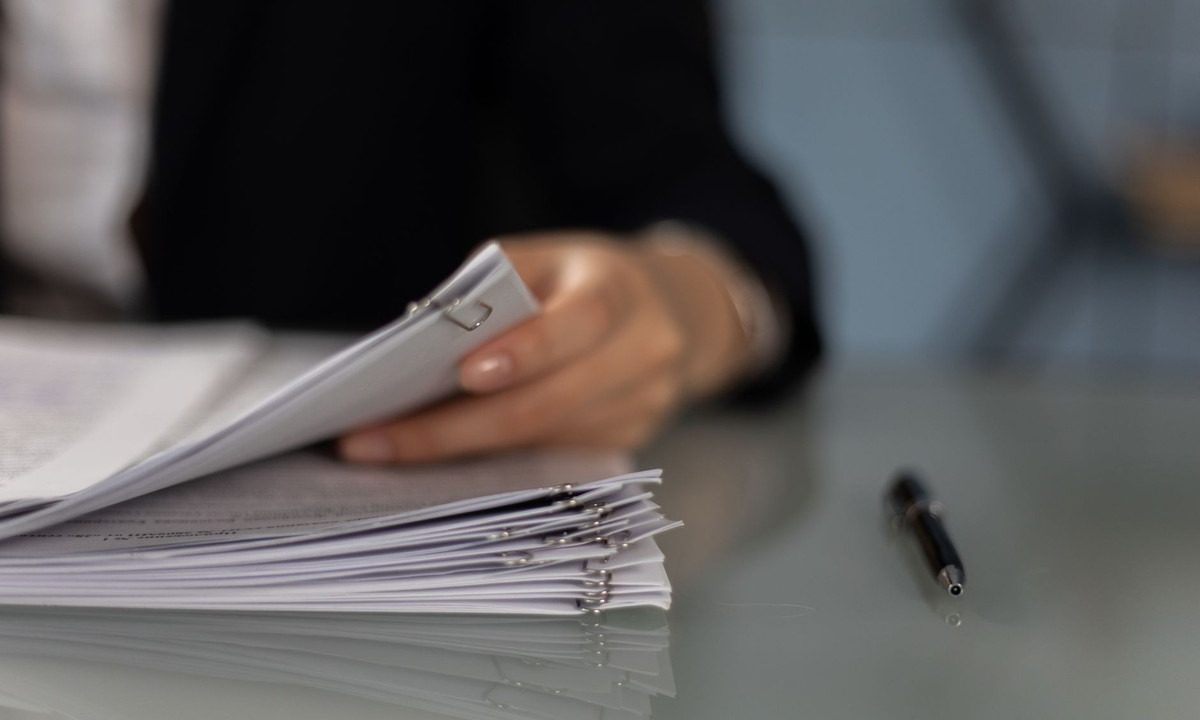 Main tenant classeur de documents sur table, stylo à côté